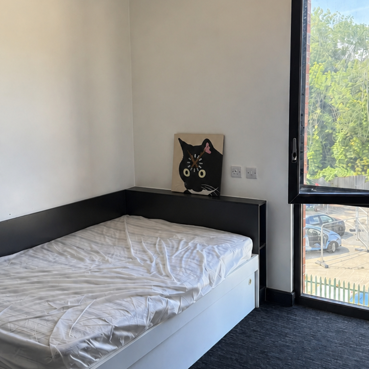 Black cat clock above a single bed in a compact studio flat